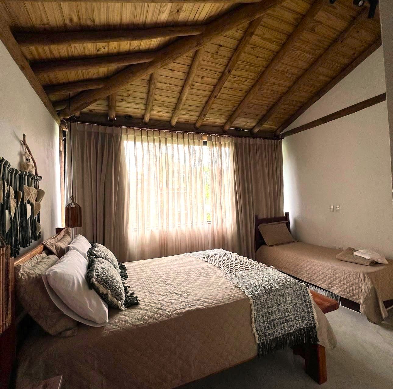 Quarto amplo da Casa Bem Bahia com teto de madeira e duas camas